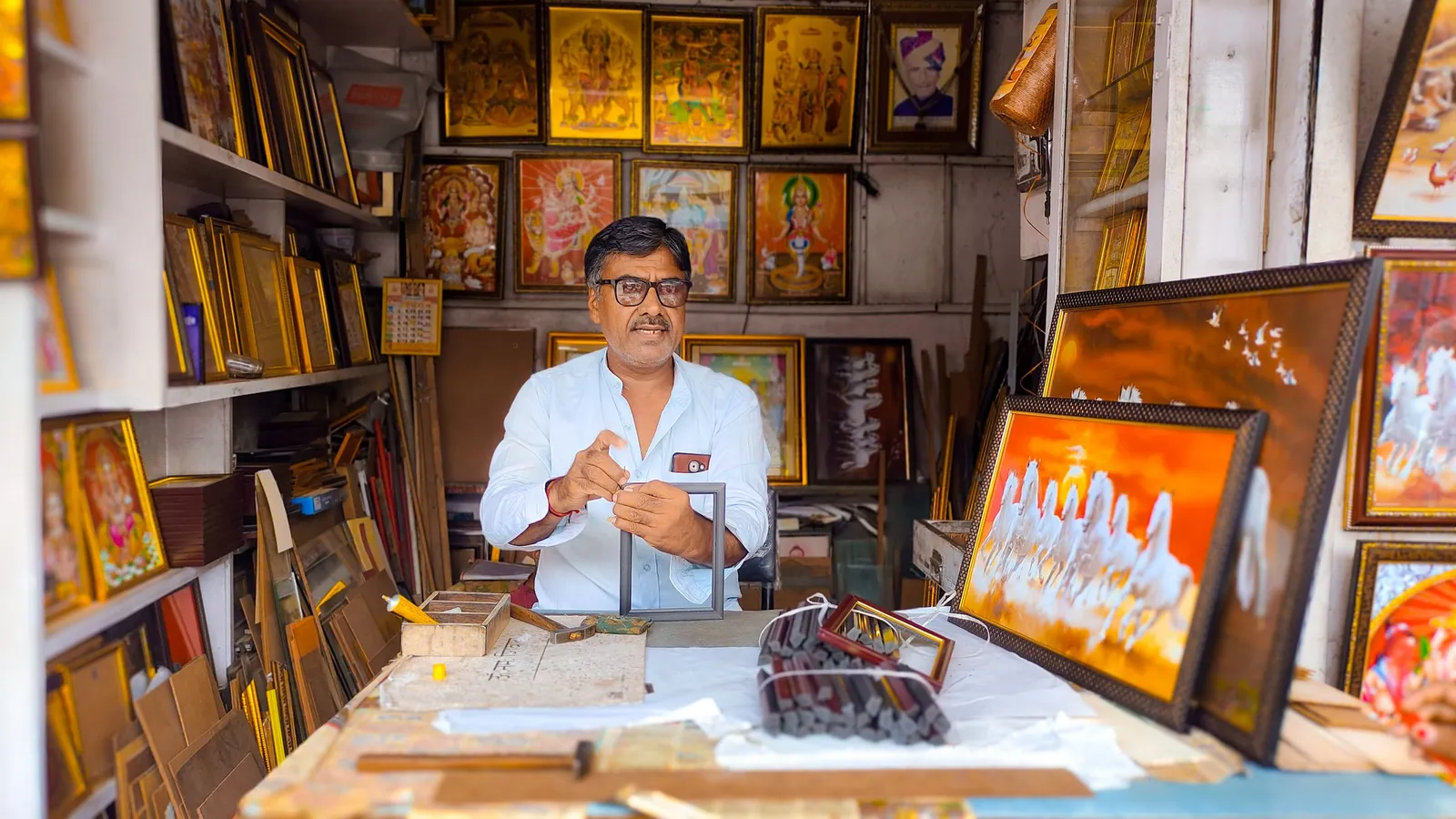 A shop owner sits at his counter in a picture-framing shop in Jodhpur, with frames all around him.