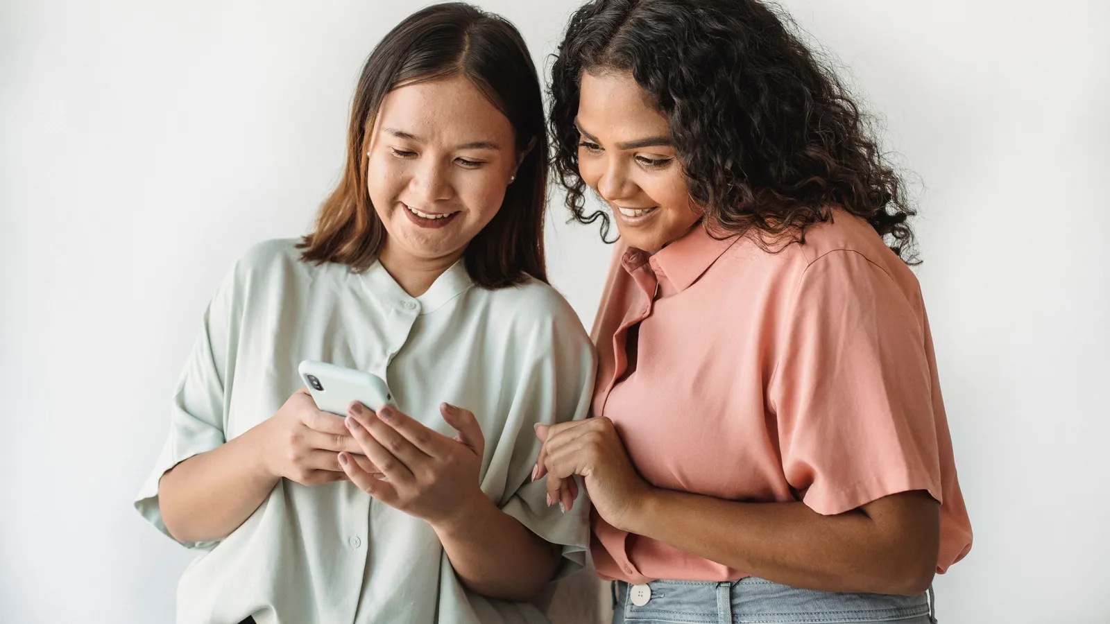 Two young women smile as they look at a phone together.