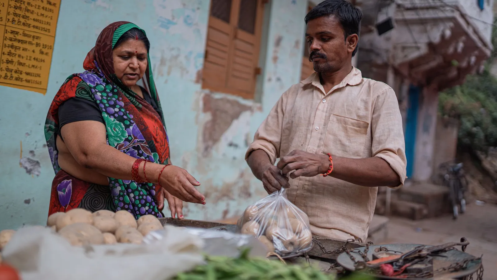 A woman and a vendor exchange vegetables across a market stall in Varanasi.
