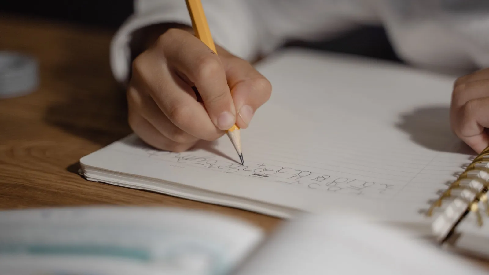 A close-up of a hand writing with a pencil in a spiral notebook.
