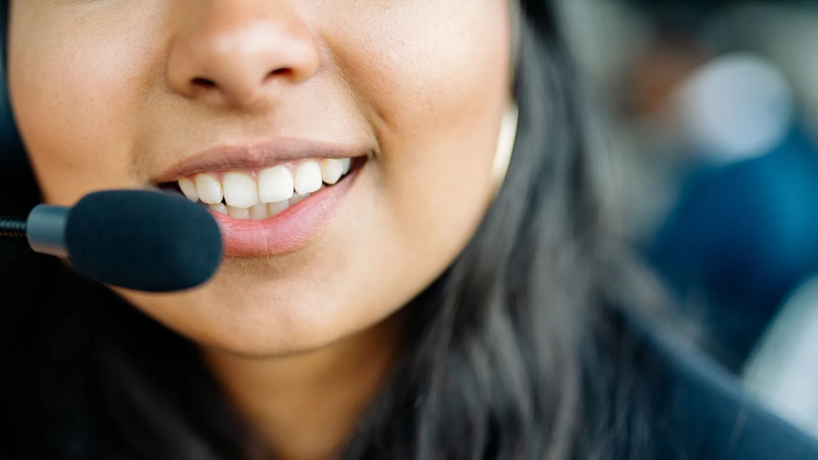 A close-up of a smiling South Asian woman's mouth as she speaks into a headset microphone.